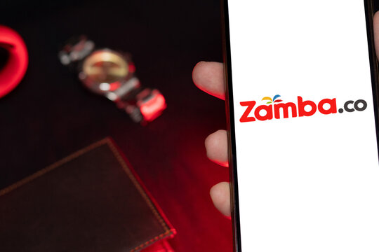 Phone with the Zamba.co logo held in front of a wallet and wristwatch, representing online sports betting and prediction games