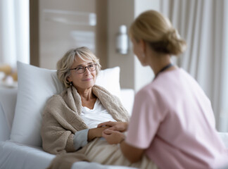 Fototapeta premium Nurse Comforting Elderly Female Patient Lying in Hospital Bed.