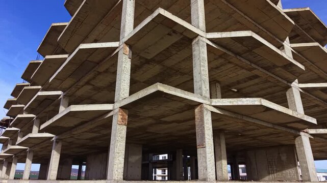 A unique view reveals an incomplete concrete building standing tall amidst a tranquil setting. The strong geometric lines and open spaces create an intriguing atmosphere of potential.