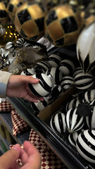 Vertical mobile photo. Female hand selects glass Christmas tree decoration, bauble with black and white stripe, ball, toy for winter holiday in supermarket, mass market shop. New Year eve, sale, gift