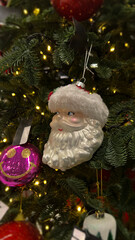 Vertical mobile photo. Glass Happy New Year toy, Santa Claus head on Christmas tree branch in mass market store, supermarket, shop. Concept of Merry Christmas eve, shopping, gift, winter holiday