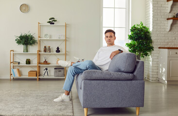 Handsome single man at home relaxing on new sofa to relax, spending good weekend alone in cozy...