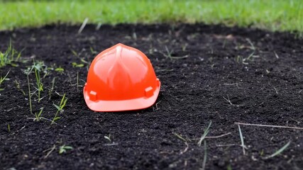 a construction orange safety helmet resting on dark soil with grass visible in the blurred background showcases workplace safety measures and preparation