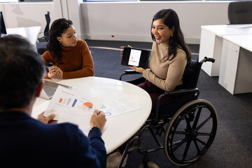 Diverse coworkers discussing data around oval table at office with tablet, paper charts, copy space
