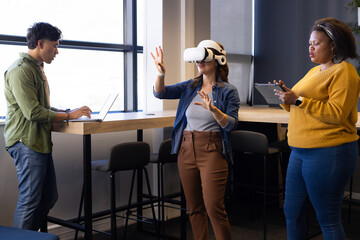 Diverse coworkers testing virtual reality demo in office lounge using laptop tablet and VR headset