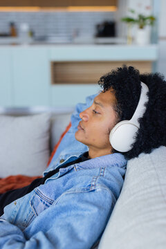 African American male reclining on couch in living room wearing denim jacket and headphones