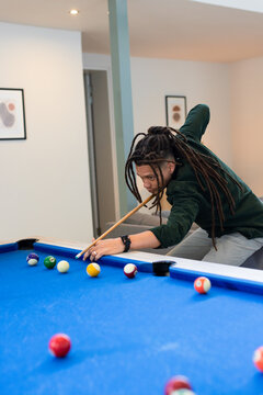 African American man leaning over blue pool table aiming cue stick at cue ball in basement