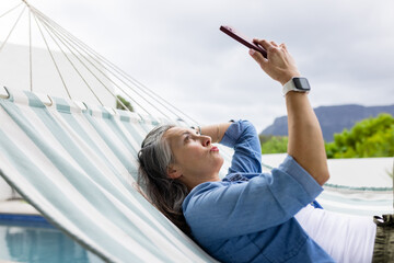 Striped hammock swinging beside poolside patio, holding red smartphone near shrubs and mountains