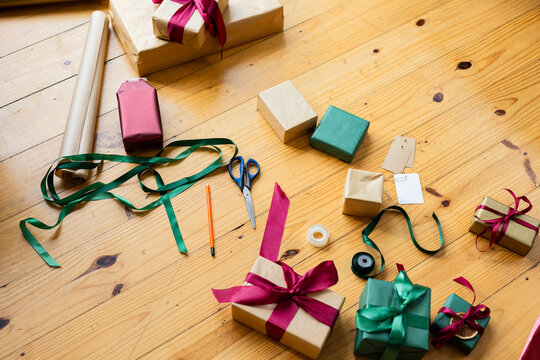 Gift box is sitting on wooden tabletop, kraft paper rolls and ribbon spools are lying nearby