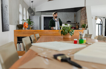 Indian man mixing paint with brush on blank canvas at work table in loft-style home studio