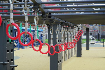 modern urban ninja warrior obstacle course with hanging rings climbing nets monkey bars and rope obstacles on soft rubber surface in public park with people training