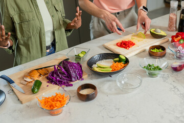 Diverse couple standing at kitchen island slicing avocado on cutting board with chef's knife
