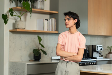 Hispanic man leaning against marble counter in home kitchen near wood shelves with books and plants