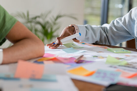 Diverse coworkers passing whiteboard marker at office table covered in colorful sticky notes