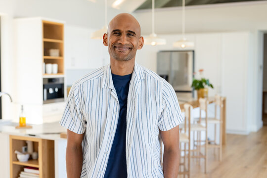 Middle-aged African American man standing and smiling in kitchen beside island with pendant lights - Powered by Adobe