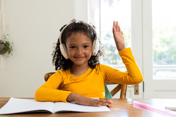 African American girl in yellow shirt writing in notebook at home study with headphones and ruler