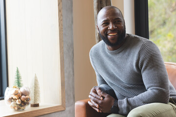 Mature African American man leaning in tan armchair at home by window with ornaments, copy space