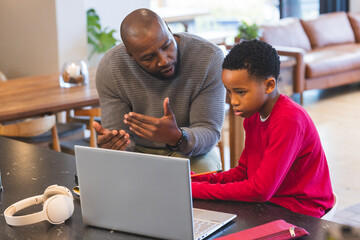 African American father and son working in living room using laptop with headphones and pencil case