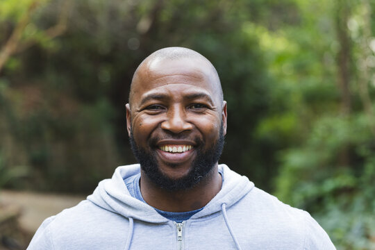 Senior African American man smiling while standing on walkway at park wearing hoodie and T-shirt