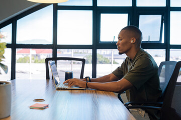 African American man typing on laptop at conference desk with coffee mug, sticky notes, copy space