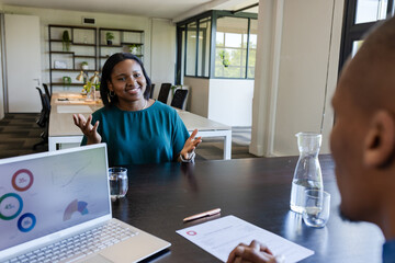 African American coworkers meeting at office, woman in teal blouse and hoops gesturing laptop