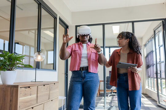 African American women colleagues, one wearing VR headset, other holding tablet, training in office