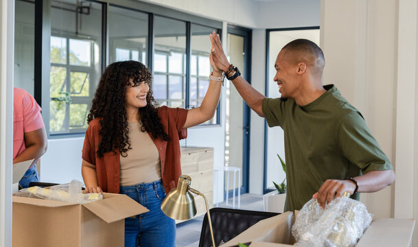 African American couple high-fiving while unpacking moving boxes at home, holding bubble wrap