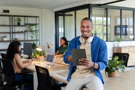 African American coworkers working at open-plan office, man holding tablet, headphones, copy space