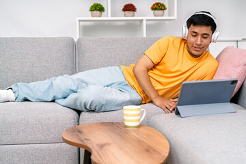 Young man working from home relaxing on sofa with tablet