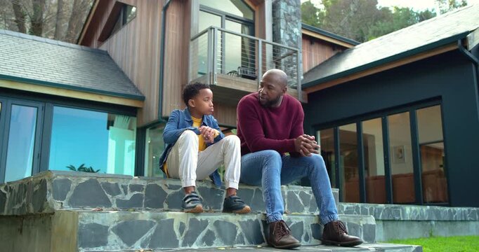 African American father and son on stone steps son fidgeting phone leading dad leaning and nodding