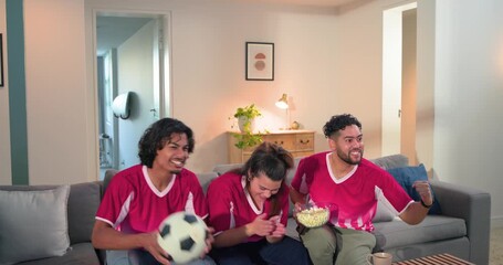 As game intensifying friends in red jerseys cheering highfiving on sofa at home with ball, popcorn