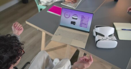 Diverse coworkers around wheelchair user discussing VR interface, gesturing at desk, copy space - Powered by Adobe