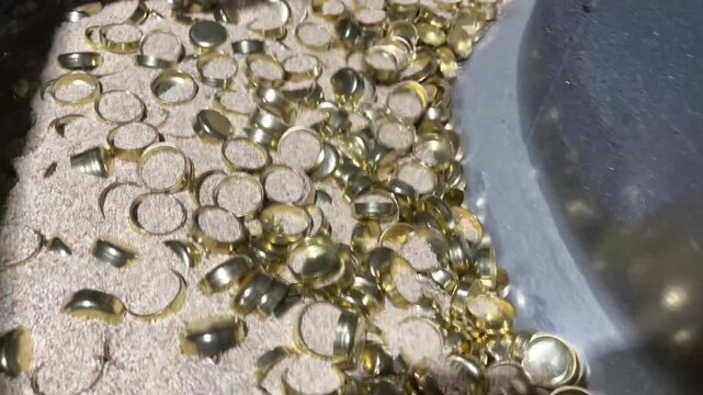 Deburring process for brass parts, drying in corn sawdust, dynamic close-up of small golden metal parts tumbling in industrial polishing media.