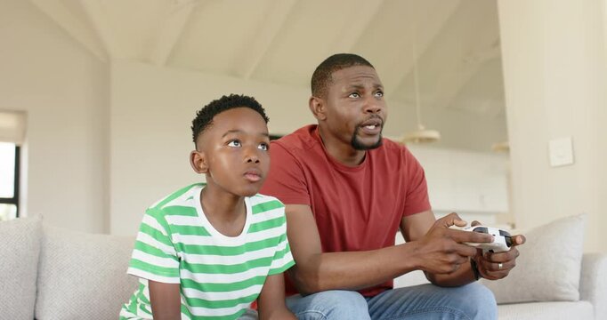 Upon second controller showing African American father and son gaming on sofa for fun