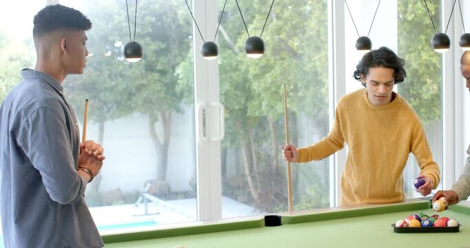 After exchanging cues, Diverse male friends in home game room racking billiard balls to start match