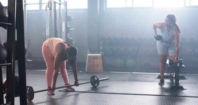 Diverse female gym partners starting set, gripping loaded barbell, rowing dumbbell at bench
