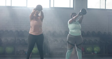 After hip hinge, diverse female workout partners swinging kettlebells upward in gym for strength - Powered by Adobe
