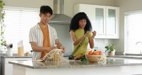 Couple unpacking reusable bags in kitchen after grocery shopping, inspecting produce for dinner - Powered by Adobe