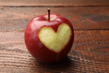 Ripe apple with carved heart on wooden table, closeup