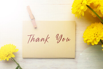 Fototapeta premium Thank You card with envelope and flowers on white wooden table, top view
