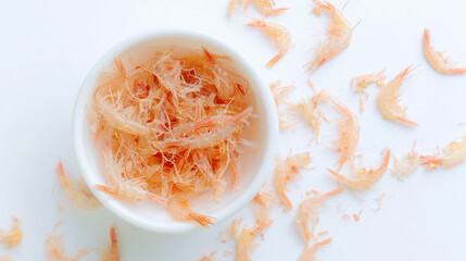 Dried small shrimp in white bowl with scattered shrimp shells on white surface, creating light and delicate seafood texture