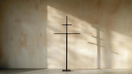 Naklejka premium Minimalist metal cross sculpture standing on a smooth floor casting soft shadows on a textured beige wall with warm sunlight creating a peaceful atmosphere