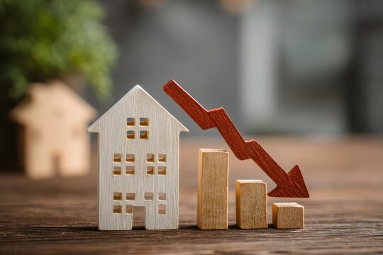 Small wooden house models with red downward arrow and bar graphs symbolizing real estate market decline or property value decrease
