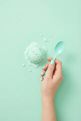 A minimal mint-green flat lay featuring a hand holding a spoon with melting mint ice cream on a matching pastel background