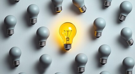 One glowing yellow light bulb standing out among multiple unlit grey light bulbs on a white background symbolizing uniqueness and innovation