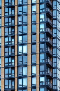 High-rise residential building facade featuring multiple windows and small balconies with blue tinted glass and light brick column details
