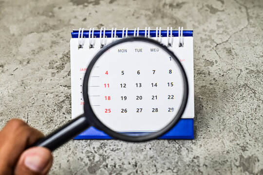 Hand holding magnifying glass on January 2026 from caledar. grey or gray cement background. Note, goal setting, future, organize, important, overview. Close up view, side. Selective focus. blue.