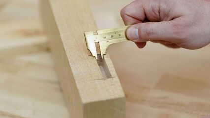 A person uses a caliper to measure a cut in a wooden block. The focus is on accuracy and craft, highlighting careful woodworking techniques in a well-lit workshop.