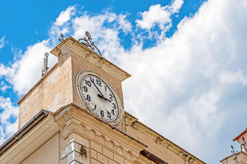 Old clock tower against a bright blue sky,showing weathered architectural details,classic round clock face,and historic building elements.In the rural Italian town Picinisco,Frosinone,Lazio.