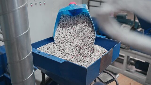 flow of processed rubber granules filling blue machinery hopper